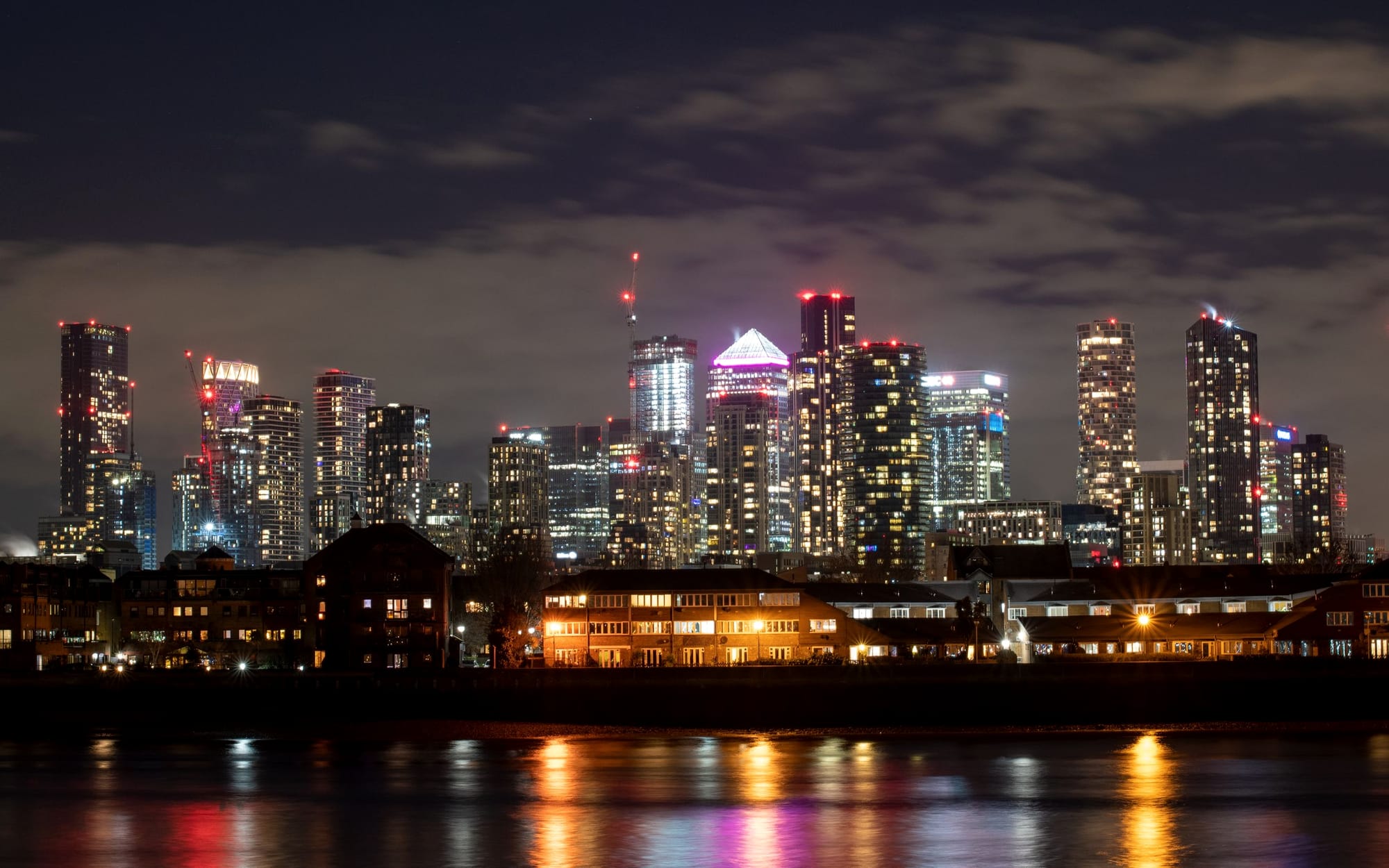 The Canary Wharf towers at dusk, their lit windows reflected in the dock water