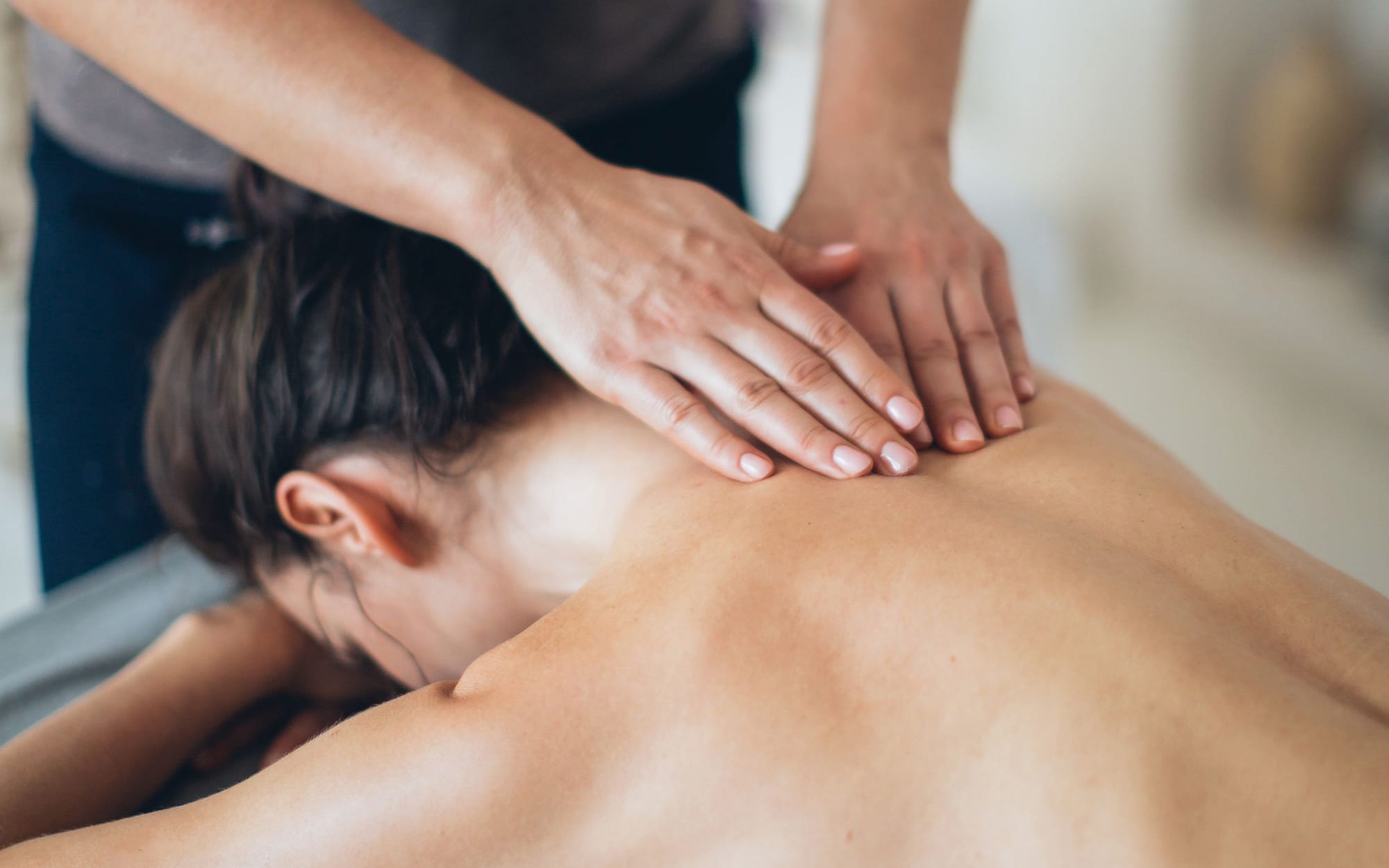 A therapist using firm forearm pressure along a client's shoulder blade in low light