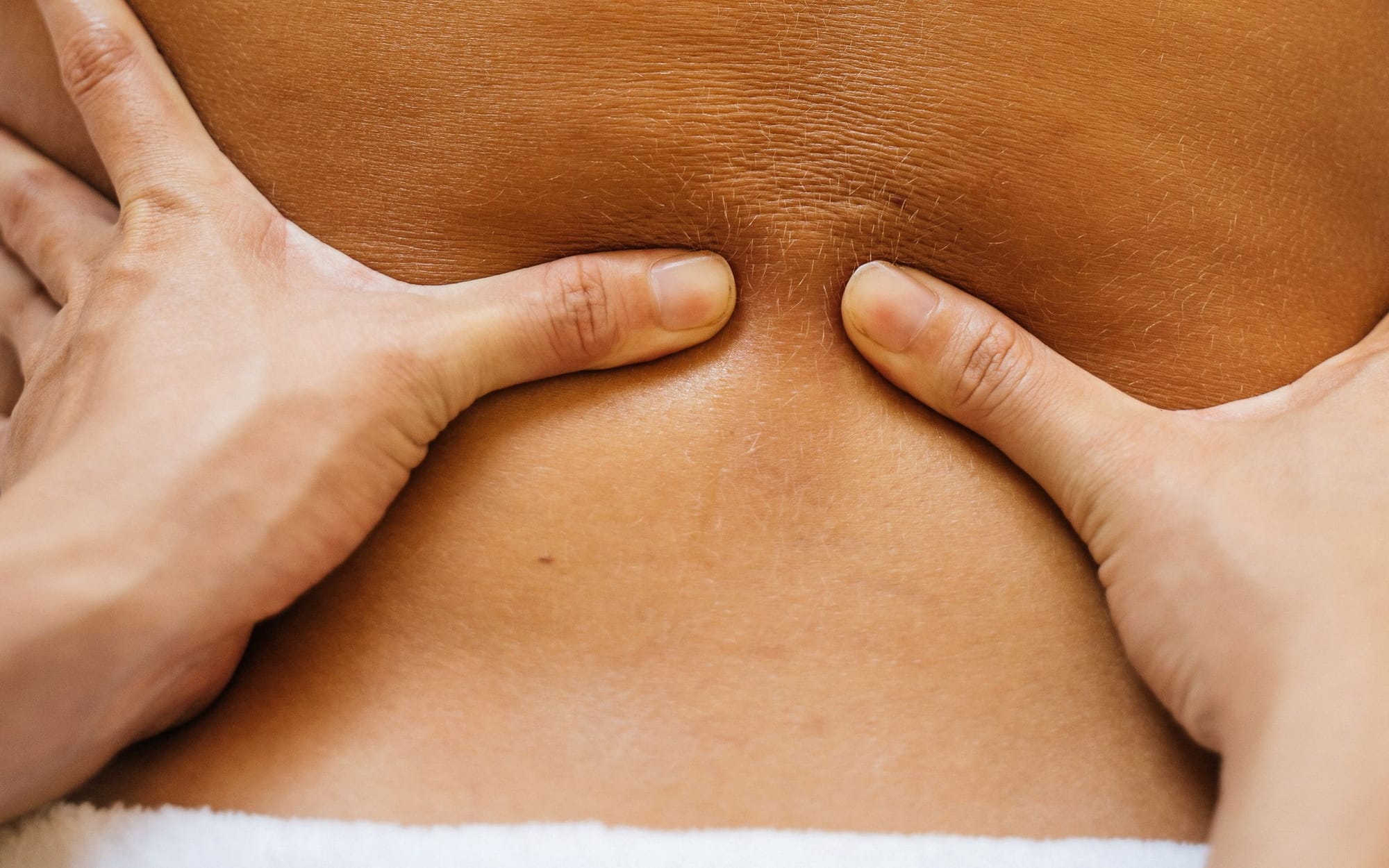 A therapist's hands working across a client's upper back in low, warm light