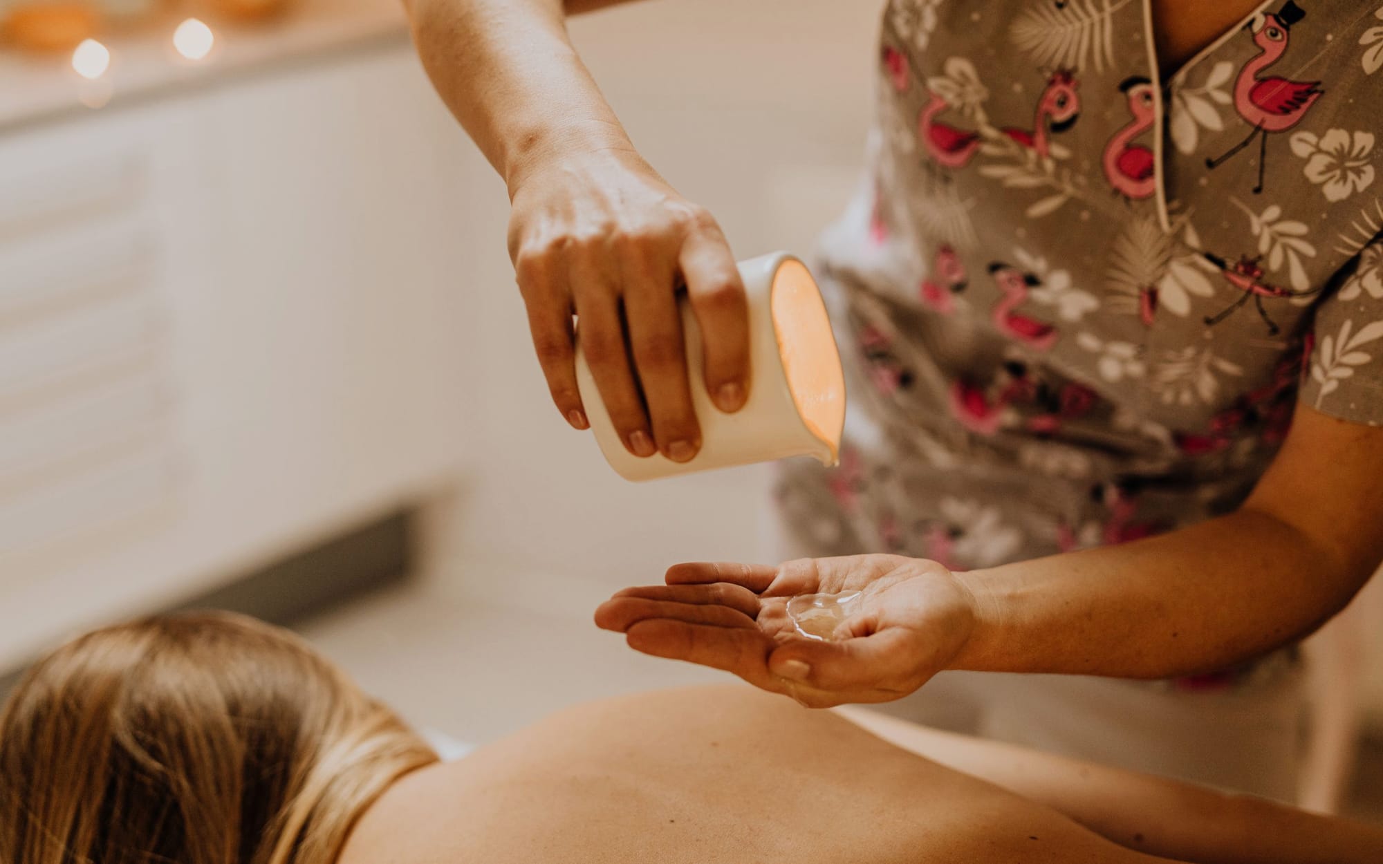 Massage oil being poured into a cupped hand beside folded towels